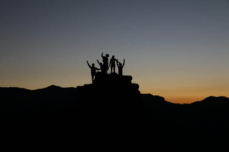 Leadership isn't Given, it's Earned. Group of People at the top of a mountain at sunset - be a better leader